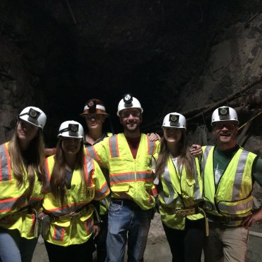EES Students wearing fluorescent vests and hardhats in front of a cave