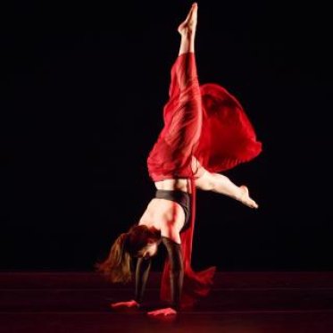 A woman dressed in red doing a handstand during a dance performance