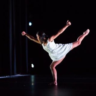 A woman dressed in white in the middle of a dance pose, standing on one leg 