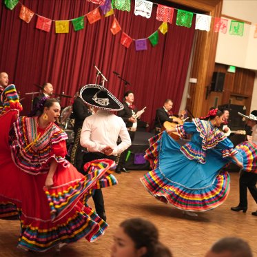 A group shot of two pairs of BFG dancers, circling each other, as a mariachi band dressed in black plays behind them at the Soda Center