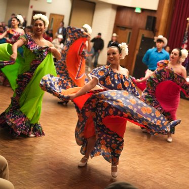 Three multi-colored BFG dancers swirl their skirts while dancing in Moraga Room