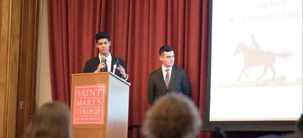 Students on stage in suits presenting at a Business Administration Case Competition