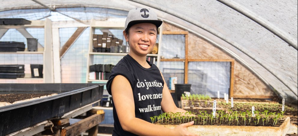 A student with a tray of seedlings wearing a shirt that says do justice love more walk humbly